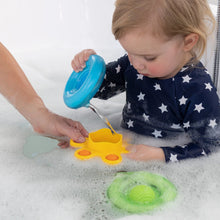 Load image into Gallery viewer, A toddler pours water using Dimpl Splash bath toys by Fat Brain Toy Co, enhancing fine motor skills in a bubble-filled bathtub.