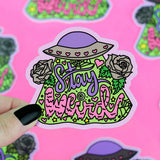 The Turtle Soup Stay Weird vinyl sticker features vibrant text, a hat, roses, hearts, and greenery held by a hand with black nails.