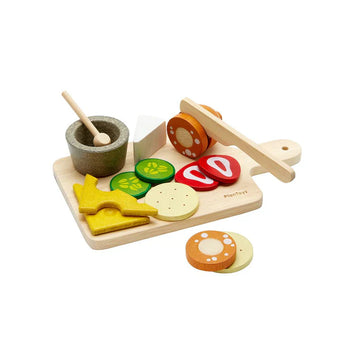 Charcuterie Board: wood cutting board with PlanToys logo, wood veggie, meat, and cheese slices, and wood knife, mortar, & pestle.