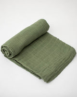 A Little Unicorn Cotton Swaddle in Fern is rolled up on one end and laid flat on a white surface.