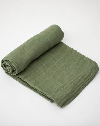 A Little Unicorn Cotton Swaddle in Fern is rolled up on one end and laid flat on a white surface.