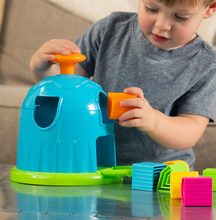 Load image into Gallery viewer, A child in a gray shirt plays with the Fat Brain Toy Co Shape Factory, enhancing spatial reasoning with colorful blocks and a shape-sorting puzzle.