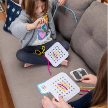 Load image into Gallery viewer, Two girls on a couch enjoy the creative fun of Sew Fast by Fat Brain Toy Co, threading strings through pegboards and tackling challenge cards.