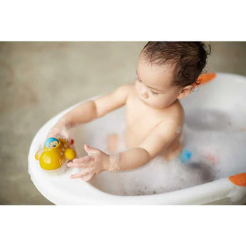 A baby delights in a PlanToys Wooden Submarine Bath Toy amidst a sea of soap bubbles.