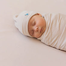 Load image into Gallery viewer, A sleeping baby lies peacefully in the Soft Knit Swaddle and Hat Set, Soft Blush by Little Unicorn, wrapped snugly on a soft surface.