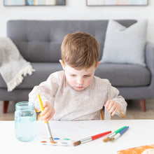 Load image into Gallery viewer, In a bright room with a gray sofa, a child paints at a white table while wearing a Bumkins Long-Sleeved Art Smock: Wander.