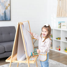Load image into Gallery viewer, A girl with a bow in her hair paints at an easel, wearing a Bumkins Long-Sleeved Art Smock: Wander, in a cozy living room.