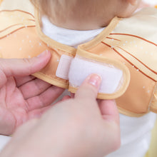 Load image into Gallery viewer, Adult hands fasten the hook-and-loop closure of a Bumkins Ruffle Apron Bib: Belle around a child's neck.