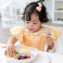 Load image into Gallery viewer, A toddler in a high chair wearing a Bumkins Ruffle Apron Bib: Belle holds a spoon and eats from a beige divided plate of pasta and berries.