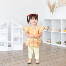Load image into Gallery viewer, A young girl stands in a bright playroom, wearing a Bumkins Ruffle Apron Bib: Belle.