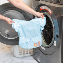 Load image into Gallery viewer, A person holds a Bumkins Ruffle Apron Bib: Cinderella in front of an open front-loading washing machine.