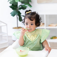 Load image into Gallery viewer, A young girl wears a Bumkins Ruffle Apron Bib: Tiana in a high chair, eating yogurt and berries from a green bowl with a spoon.