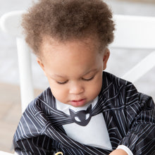 Load image into Gallery viewer, A young child wearing a Bumkins Sleeved Bib: Jack Skellington, looking down with a serious expression.