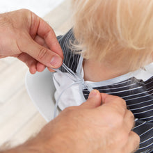 Load image into Gallery viewer, An adult ties the ribbon closure of a Bumkins Sleeved Bib: Jack Skellington around a blonde child's neck.