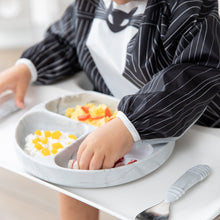 Load image into Gallery viewer, A child enjoys eating with their hands from a divided plate while wearing a Bumkins Sleeved Bib: Jack Skellington.