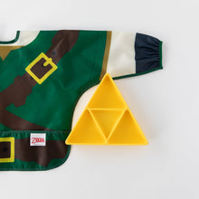 Load image into Gallery viewer, Bumkins Sleeved Bib: Zelda™ lays flat next to a yellow triangle-shaped divided plate on a white background.