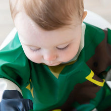 Load image into Gallery viewer, A serene baby with light hair looks down, wearing a Bumkins Sleeved Bib: Zelda™.