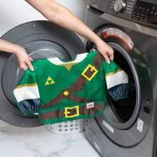Load image into Gallery viewer, A person holds a Bumkins Sleeved Bib: Zelda™ in front of an open front-loading washing machine.