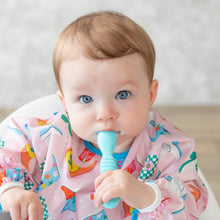 Load image into Gallery viewer, A baby girl with bright eyes in a pink patterned bib holds a Bumkins Silicone Dipping Spoons 3 Pack: Gumdrop in her mouth.