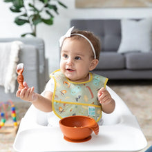 Load image into Gallery viewer, A baby in a high chair, with a white bow, eats from a Bumkins Silicone First Feeding Set: Clay in a cozy living room.
