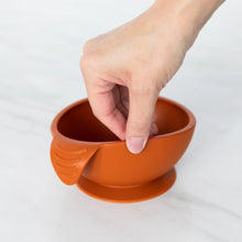 Load image into Gallery viewer, A hand holds a Bumkins Silicone First Feeding Set: Clay, demonstrating the suction cup bottom on a marble surface.