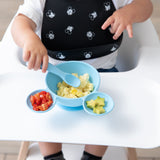 A toddler in a high chair eats scrambled eggs, tomatoes, and avocado from a Bumkins Silicone First Feeding Set: Mickey Mouse Light Blue.