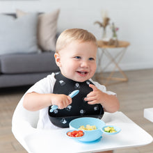 Load image into Gallery viewer, A toddler in a high chair smiles, eating from Bumkins Silicone First Feeding Set: Mickey Mouse Light Blue with chopped tomatoes and avocado.