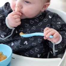 Load image into Gallery viewer, A baby in high chair wearing a patterned bib eats from Bumkins Silicone First Feeding Set: Mickey Mouse Light Blue.