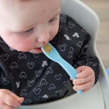 Load image into Gallery viewer, A baby in a high chair wears a bib, holding a spoon from Bumkins Silicone First Feeding Set: Mickey Mouse Light Blue.