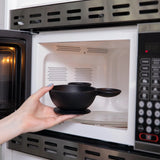 A hand places a Bumkins Silicone First Feeding Set: Mickey Mouse Classic Black into an open microwave.