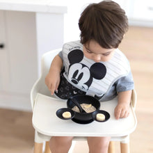 Load image into Gallery viewer, A toddler enjoys breakfast in a high chair from Bumkins Silicone First Feeding Set: Mickey Mouse Classic Black while wearing a matching bib.