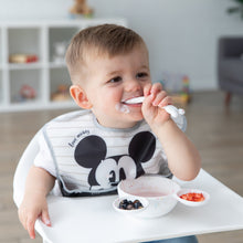 Load image into Gallery viewer, A toddler in a high chair enjoys yogurt and berries with a spoon from a Bumkins Silicone First Feeding Set: Mickey Mouse Vanilla Sprinkle.