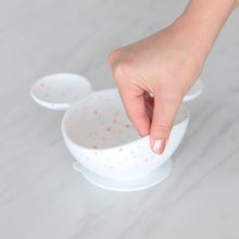 Load image into Gallery viewer, A hand lifts a Bumkins Silicone First Feeding Set: Mickey Mouse Vanilla Sprinkle on a marble surface, showcasing the suction cup bottom.