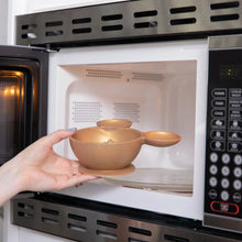 Load image into Gallery viewer, A person places Bumkins Silicone First Feeding Set: Minnie Mouse Gold filled with food into an open microwave.