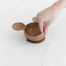 Load image into Gallery viewer, A hand holds a Bumkins Silicone First Feeding Set: Minnie Mouse Gold, demonstrating the suction cup bottom on a marble surface.
