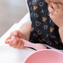Load image into Gallery viewer, Close-up of a baby self-feeding with a Bumkins Silicone First Feeding Set: Minnie Mouse Light Pink, with food adorably smeared on tiny fingers.
