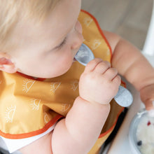 Load image into Gallery viewer, Close-up of a baby wearing a yellow bib chewing the spoon of a Bumkins Silicone First Feeding Set: Gray.