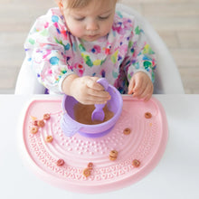Load image into Gallery viewer, A baby in a floral bib eats from a Bumkins Silicone First Feeding Set: Lavender surrounded by cereal on a pink silicone mat.