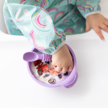 Load image into Gallery viewer, Close-up of a child in a colorful bib using a Bumkins Silicone Dipping Spoons 3 Pack: Lollipop to eat yogurt & berries from a purple bowl.