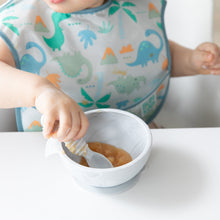 Load image into Gallery viewer, Close-up of a child in a dinosaur print bib eating applesauce from a bowl with a Bumkins Silicone Dipping Spoons 3 Pack: Taffy.