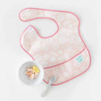 A pink floral bib lays next to Bumkins Silicone First Feeding Set: Marble with shrimp and lemon on a white background.