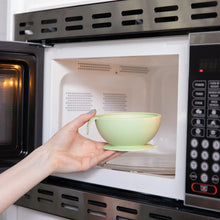 Load image into Gallery viewer, A person places a Bumkins Silicone First Feeding Set: Sage into an open microwave.