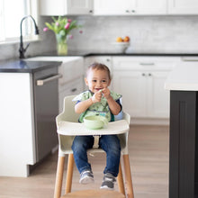 Load image into Gallery viewer, A toddler in a green bib smiles in a high chair, eating from a Bumkins Silicone First Feeding Set: Sage in a bright kitchen.