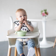 Load image into Gallery viewer, A baby in a high chair wearing a black & white patterned bib enjoys mealtime with Bumkins Silicone First Feeding Set: Sage.