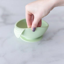 Load image into Gallery viewer, A hand holds a Bumkins Silicone First Feeding Set: Sage, demonstrating the suction cup bottom on a marble surface.