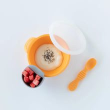 Load image into Gallery viewer, A gray cup of diced fruit sits on a Bumkins Silicone First Feeding Set: Tangerine filled with yogurt and chia seeds on a marble background.