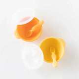 Bumkins Silicone First Feeding Set: Tangerine sits next to a yellow bowl and spoon set on a white background.