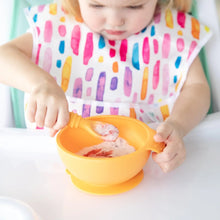 Load image into Gallery viewer, A child wearing a colorful bib sits in a high chair, eating from a Bumkins Silicone First Feeding Set: Tangerine.