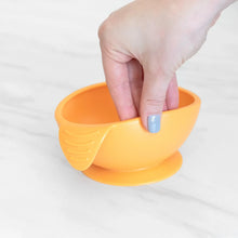 Load image into Gallery viewer, A hand holds a Bumkins Silicone First Feeding Set: Tangerine, demonstrating the suction cup bottom on a marble surface.
