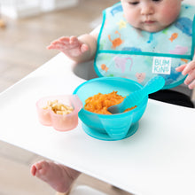 Load image into Gallery viewer, A baby sits in a high chair with a Bumkins Silicone First Feeding Set: Blue Jelly filled with pureed sweet potatoes near a pink cup of fruit.
